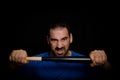 Bearded man dressed in blue t-shirt in defiant pose posing whit a baseball bat on black background Royalty Free Stock Photo