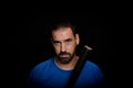 Bearded man dressed in blue t-shirt in defiant pose posing whit a baseball bat on black background Royalty Free Stock Photo