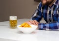 Bearded man drinks beer and eats chips in the kitchen, junk food Royalty Free Stock Photo