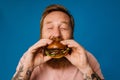 Bearded man eating burger while standing isolated over blue background