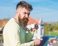 Bearded man with espresso mug, drinks coffee. Man with beard and mustache on strict face drinks coffee, urban background Royalty Free Stock Photo