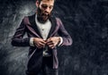 A young bearded man with expressive style buttoning his elegant jacket standing against a dark textured wall Royalty Free Stock Photo