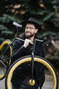 Bearded man with a fixie bicycle. Low angle view of confident young bearded man carrying his bicycle on shoulder and looking at