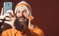 Bearded man in funny hat taking selfie with his smartphone. Photographer hobby. Selfie time. Cheerful man makes self Royalty Free Stock Photo