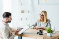 Bearded man gesturing while holding clipboard near recruiter in glasses