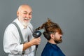 Bearded man getting hairstyle by hairdresser with hair dryer at barbershop. Funny hairdresser holding a blow dryer.