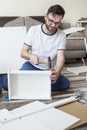 Bearded man in glasses, a white T-shirt and jeans sits on a carpet in the living room and twists furniture. He holds the hammer an Royalty Free Stock Photo