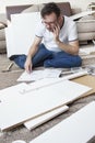 Bearded man in glasses, a white T-shirt and jeans sits on the rug thoughtfully and reads the furniture assembly instructions. Th Royalty Free Stock Photo