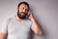 Bearded man in gray t-shirt holding mobile phone, using smartphone, making a call Royalty Free Stock Photo