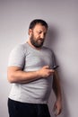 Bearded man in gray t-shirt holding mobile phone, using smartphone, making a call Royalty Free Stock Photo