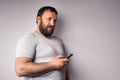Bearded man in gray t-shirt holding mobile phone, using smartphone, making a call Royalty Free Stock Photo