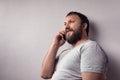 Bearded man in gray t-shirt holding mobile phone, using smartphone, making a call, talking on the phone Royalty Free Stock Photo