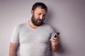 Bearded man in gray t-shirt holding mobile phone, using smartphone, making a call Royalty Free Stock Photo