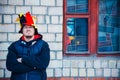 Bearded man in the hat of a buffoon stands near the brick wall