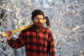 Bearded man with a hatchet, forestry. Handsome man, hipster in snowy forest. Lumberjack in the woods with an ax on