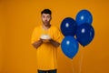 Bearded man holding birthday cake and blowing out candles while standing with blue air balloons isolated Royalty Free Stock Photo