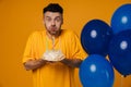 Bearded man holding birthday cake and blowing out candles while standing with blue air balloons isolated Royalty Free Stock Photo