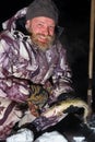 Bearded man is holding fish and smiling at dark winter night