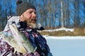 Bearded man is holding frozen fish after successful winter fishing at cold sunny day Royalty Free Stock Photo