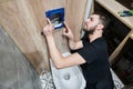 Male plumber installing toilet flush system in bathroom.