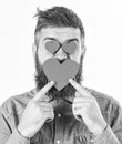 Bearded man holds symbols of love. Hipster with paper red hearts on his face. Mature handsome man in love. Macho with