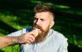 Bearded man with ice cream cone. Man with long beard eats ice cream, while sits on grass. Man with beard and mustache on