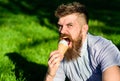 Bearded man with ice cream cone. Temptation concept. Man with long beard eats ice cream, while sits on grass. Man with