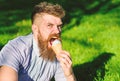 Bearded man with ice cream cone. Temptation concept. Man with long beard eats ice cream, while sits on grass. Man with Royalty Free Stock Photo