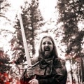 Battle cry, battle. Knight in the forest. Guy in medieval costume with sword. effect of fire and toning Royalty Free Stock Photo