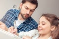 Father and little daughter at home sitting at table girl doing assignment while father looking after Royalty Free Stock Photo