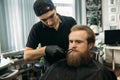 Bearded man with long beard getting stylish hair shaving , haircut , with razor by barber in barbershop Royalty Free Stock Photo