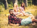 Bearded man in lumberjack shirt spending time with friends outdoors. Handsome man lying on glass in woods. Outdoor