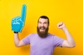 Bearded man is making the winner gesture while wearing foam fan glove. Royalty Free Stock Photo