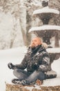 Bearded man meditates sitting on a snowy fountain while is snowing