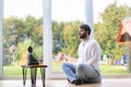 Bearded man meditating cross legged sitting on a pillow in front of a buddha statue.