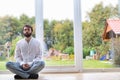 Bearded man meditating cross legged sitting on a pillow in front of a buddha statue.