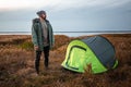 A bearded man near a camping tent in green on the background of nature and the lake. The concept of travel, tourism, camping Royalty Free Stock Photo