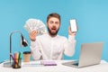 Bearded man office worker looking at camera with astonishment holding big sum of dollar cash and smartphone with white display, Royalty Free Stock Photo