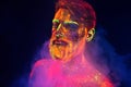 Bearded man painted in fluorescent powder on a background of smoke