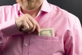 Bearded man in a pink shirt hides money in his pocket