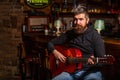 Bearded man playing guitar, holding an acoustic guitar in his hands. Play the guitar. Beard hipster man sitting in a pub