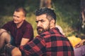 Bearded man relax with friends in forest. Hipster with long beard in plaid shirt on nature. Tourist enjoy camping