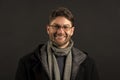 Bearded man in scarf and coat on dark background. Happy man in glasses on bearded face. Fashion model with beard smile