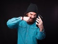 A bearded man is screaming and puching the phone that he is holding near a black wall