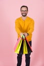 Shopping bags in hand of handsome smiled guy in glasses. Colored paper bags in hand of man in orange cardigan