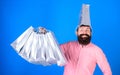 Bearded man with silly look and big smile isolated on blue background. Male shopaholic with trendy beard carrying silver