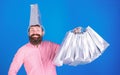 Bearded man with silly look and big smile isolated on blue background. Male shopaholic with trendy beard carrying silver