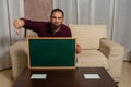 Bearded man sitting on the couch at home with a blackboard with his thumb down