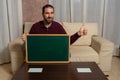 Bearded man sitting on the couch at home with a blackboard with this thumb up Royalty Free Stock Photo