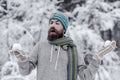 Bearded man with snowballs in snowy forest. Skincare, beard care in winter. Hipster in jacket, hat, scarf, beard warm in
